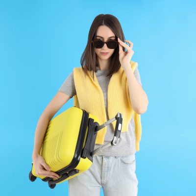 Attractive woman with travel bag on blue background
